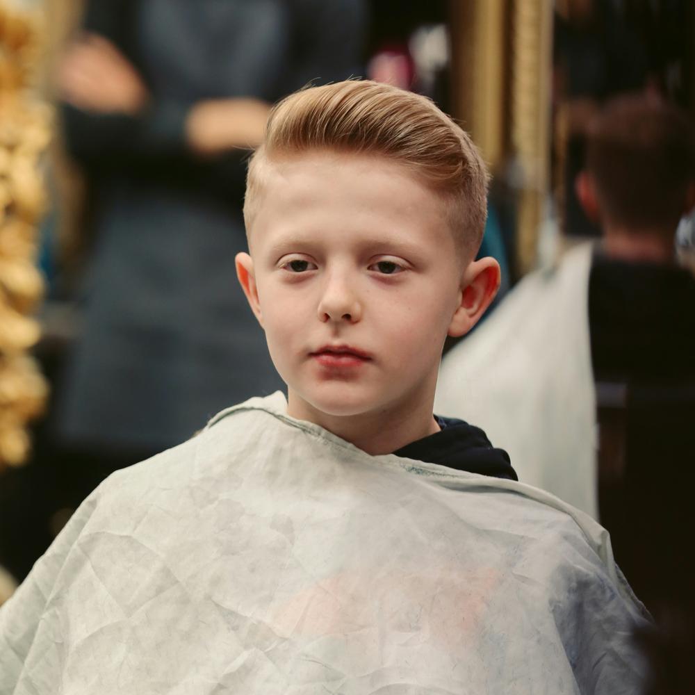 Chlapec s modern&yacute;m chlapčensk&yacute;m &uacute;česom sed&iacute; v kadern&iacute;ctve